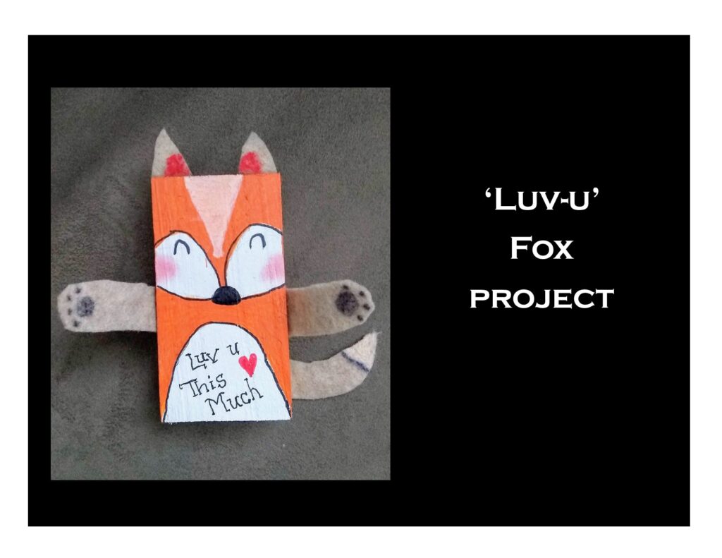 A handmade fox craft with outstretched felt arms, painted face, and the message "Luv u This Much" written on its body. The text on the side reads "'Luv-u' Fox project."