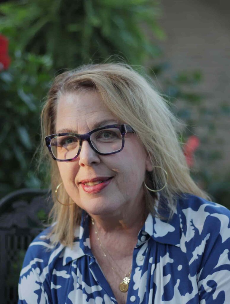 Woman with blond hair and glasses, smiling at the camera.
