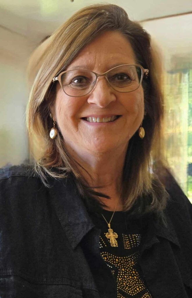 A woman in a button down jacked and glasses, smiling.