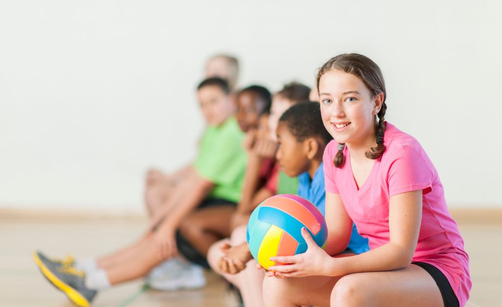 A group of children sitting in a row holding a ball ready to play team-based indoor youth group games