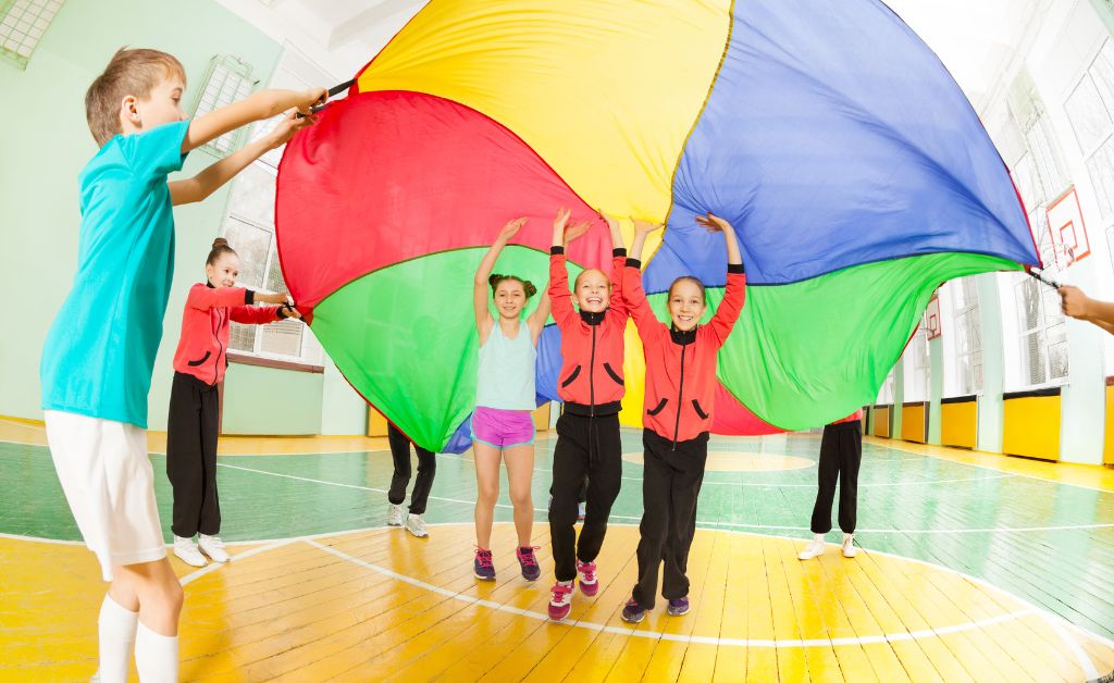Children playing a high-energy indoor group game with a colorful parachute in a gymnasium